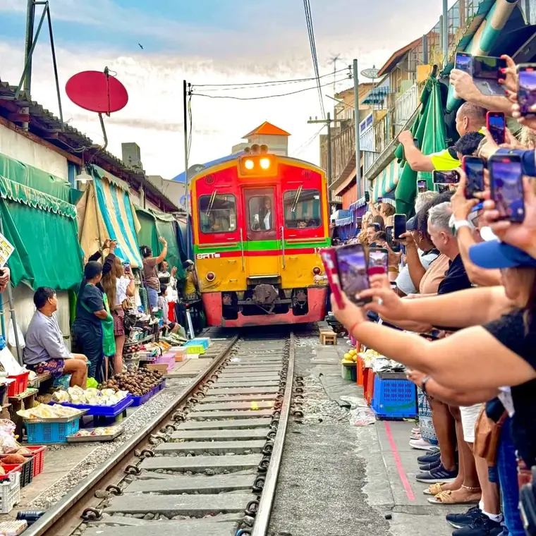 Zug im Maeklong Railway Market mit Besuchern direkt neben den Gleisen.